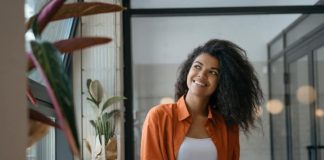 How to Find Your Brand Identity and Market It A person holding a blue pen and a notebook looking out a nearby window. The person smiles while looking outside.