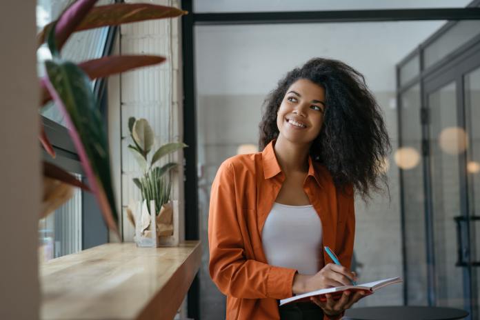 pipe and drape-402743-farmhouse-sink-kitchen-ImageA1 A person holding a blue pen and a notebook looking out a nearby window. The person smiles while looking outside.