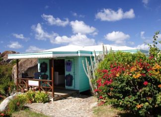 Why First Impressions Start With a Building’s Exterior A turquoise blue small Caribbean shop that's surrounded by plants on a cliff next to the beautiful ocean.