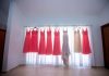 A white gown, six coral gowns, and an ivory gown all hang on a curtain rod as light shines through the sheer curtains.